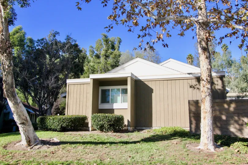 Beige townhome with brick fence and trees in the yard in Village San Juan Townhomes.