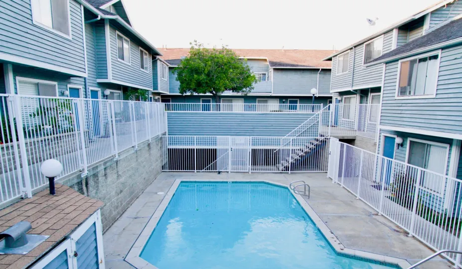 The swimming pool in the Brightwood Square with beautiful blue colored buldings, stairs and a big tree.