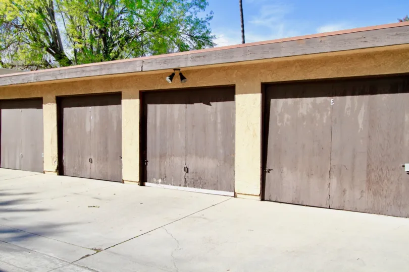 In sunny day of Fairview, two lights are connected on ceiling wall with tall greenish trees and closed car shed door
