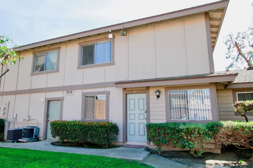 Two story Normandy Place apartment building with white doors and trimmed bushes.