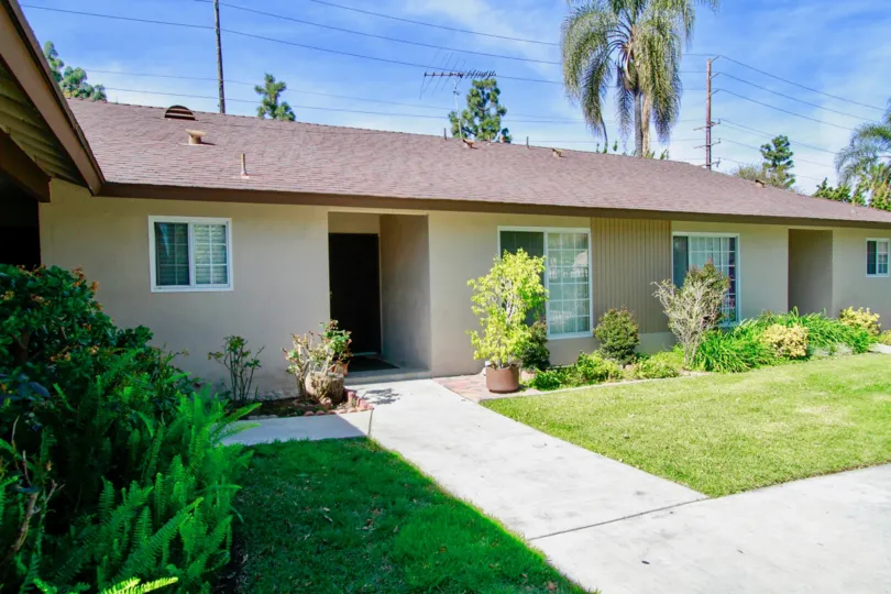 The greay color house in the Saddlebark Park Villas with a beautiful flower garden, trees, green grass and shrubs.