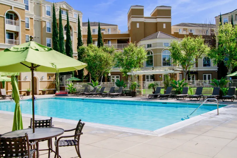 Inside the apartment in Vantage has tallest trees, swimming pool, dinning tables, seating chairs and with umbrella's