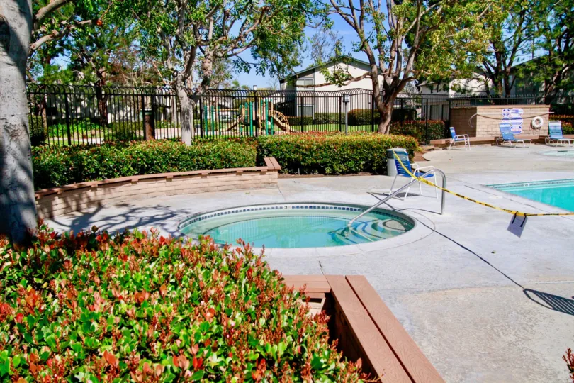 Two pools with lawn chairs around the pools with gate and park in the back in windwood forest communtiy in santa ana, california.