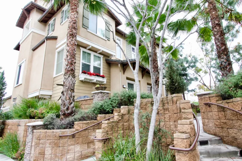 Decorative brick retaining walls with stone pathways lined by mature trees outside Arbor Walk two storey homes