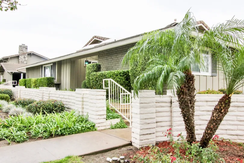 This image represents the front view of the house with the beautiful garden with trees plants and the lawn which is located in the city of Tustin