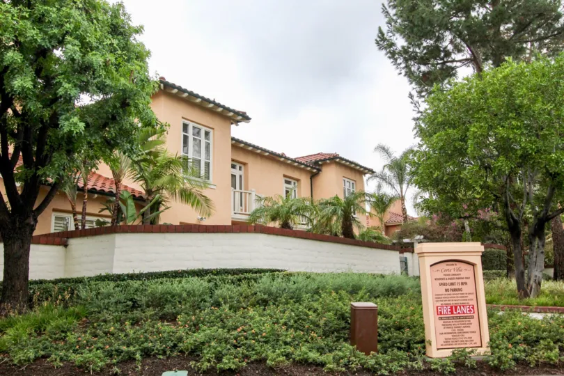 Large brick capped privacy wall and large front lawns with Fire Lane warning sign and mature trees at Corte Villa
