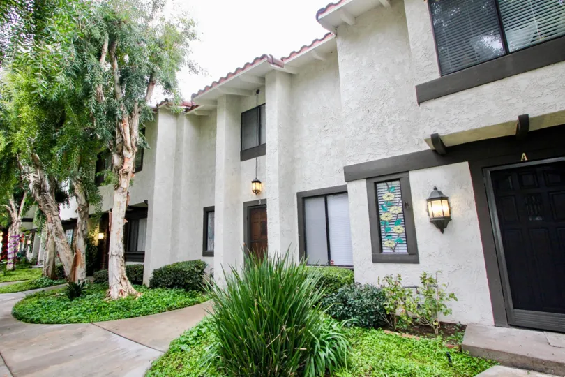 This image shows the front view of the home which have the lot of trees, plants, light lamps, glass doors are there in the city of Tustin
