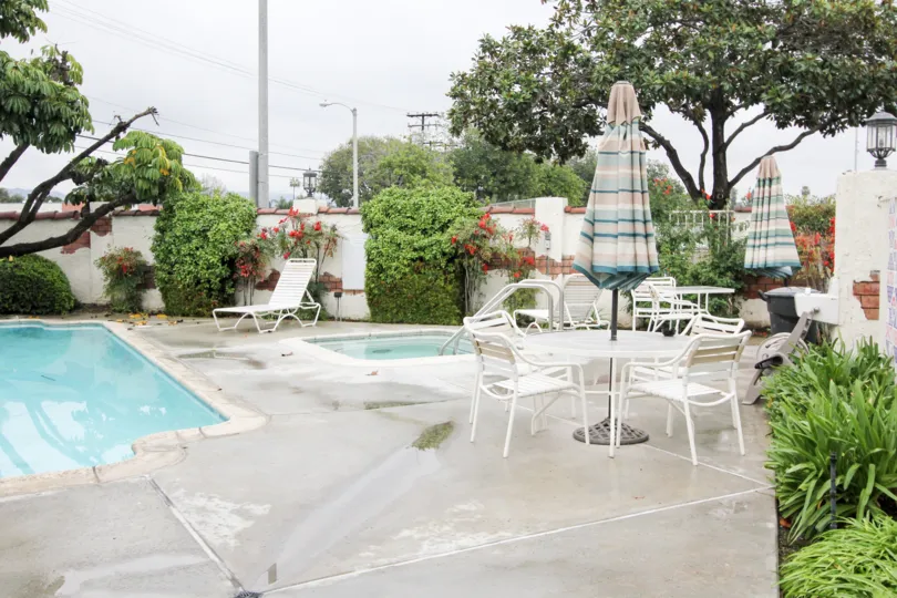 Pool area in the community of Macaw Cove in Tustin, California. Hot tub with lounge chairs and tables with umbrellas nearby,