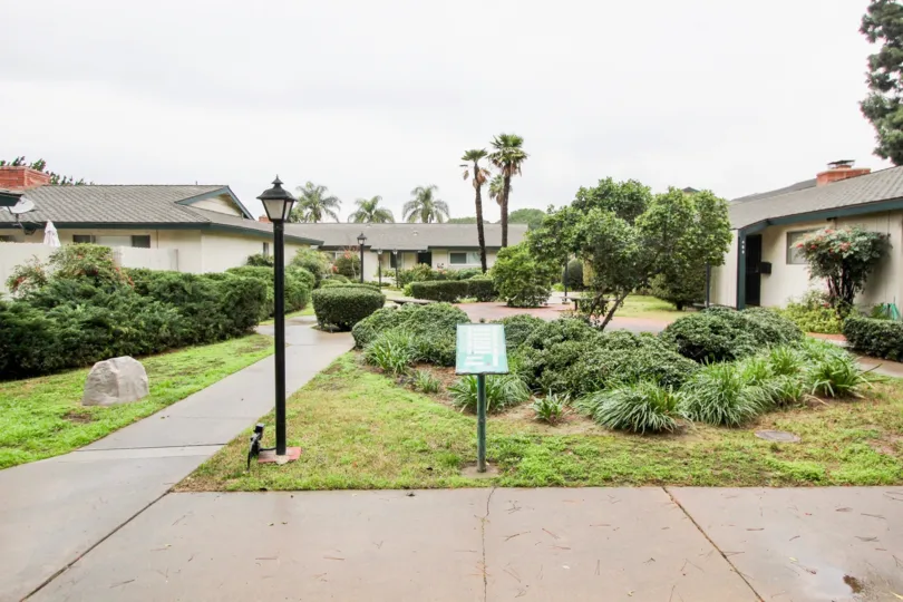 An overcast day by a Palmwood Gardens apartment complex with a light pole and information stand in the front and trees and bushes scattered about