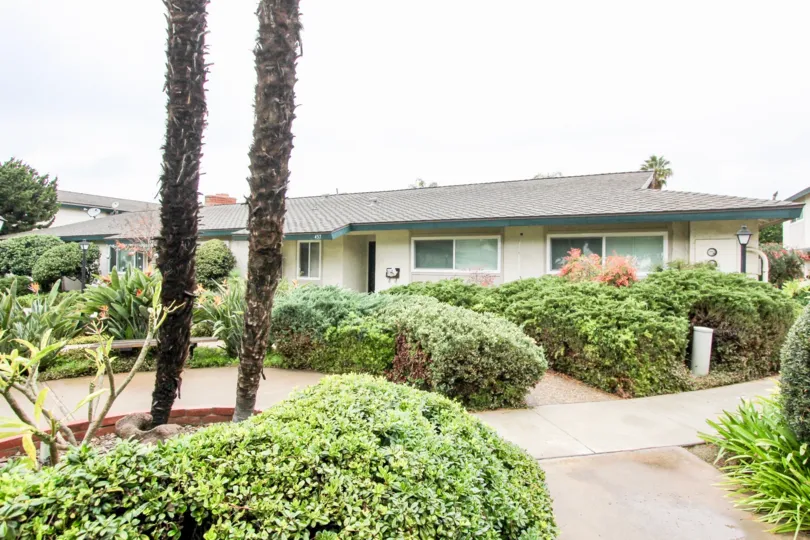 Front view of house with many bushes and plants in front on cloudy day