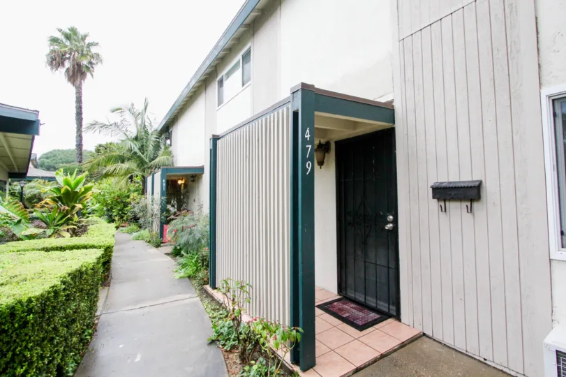 An overcast day at a Palmwood Gardens apartment complex with 1 sidewalk leading to all doors and bushes and plants on the other side of the sidewalk