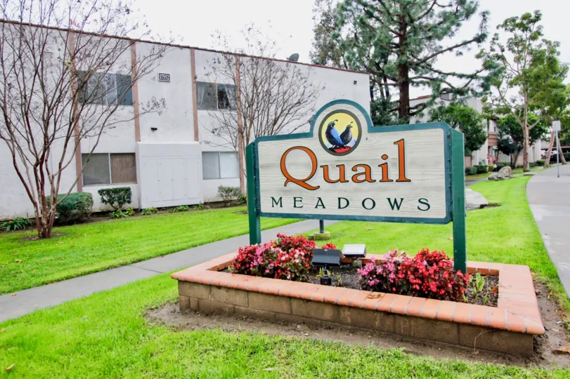 A sunny day in the area of Quail Meadows, outside, grass, condo, flowers, trees. welcome sign