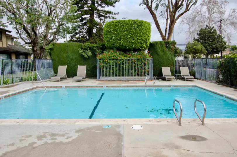 A partly cloudy day at a San Juan Meadows pool with a house(s) on one side and trees and bushes behind it
