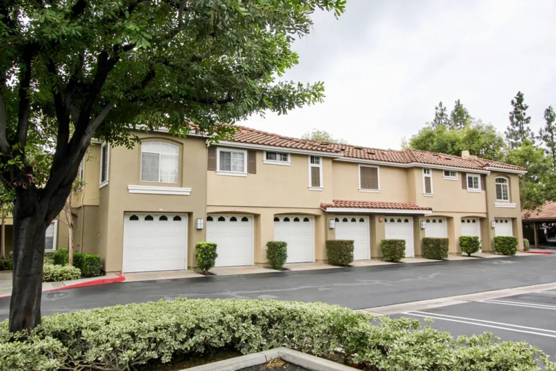 An overcast day by a Shadow Canyon multiplex with little bushes in between each garage door and other trees and plants uniformly around the area