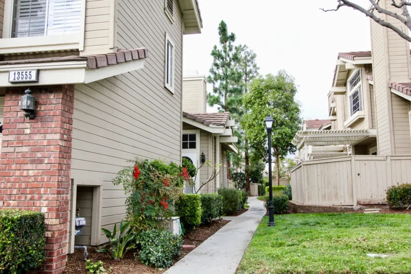 Side view of residences located in Sycamore Glen in Tustin, California. Lights are along the sidewalk leading to residences. Lots of foliage around these two story residences.