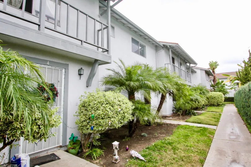 An overcast day by a Tustin Imperial complex with bushes, trees, and grass in front of each place and on both sides of the walkway