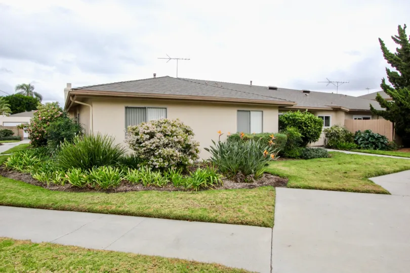 An overcast day by a Tustin Park Villas house with grass, trees, and other plants all around