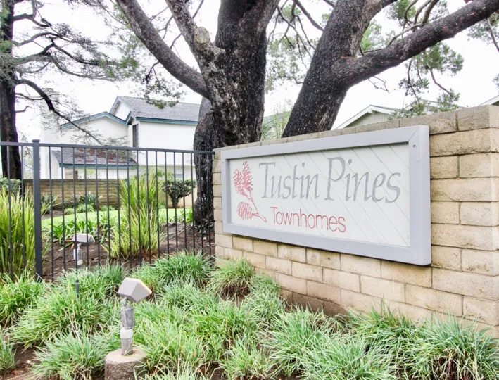 Tustin Pines Townhomes entrance sign on tan bright with mature trees, tall fencing and community landscaping