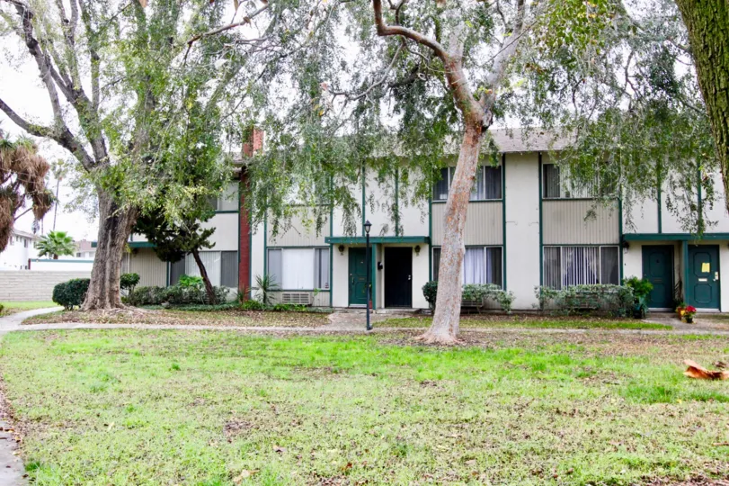 An overcast day by a Tustin Place apartment building with few bushes by it and trees scattered about