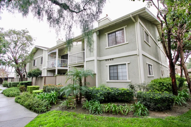 This image shows the fabulous house with the plants which have the lot of trees and plants and the pathway, glass windows, balcony in the city of tustin