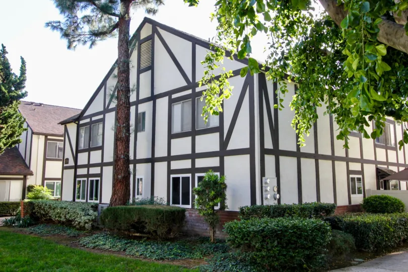 The charming Williamshire Condos with white siding, brown craftsman style trim, tall trees and common area