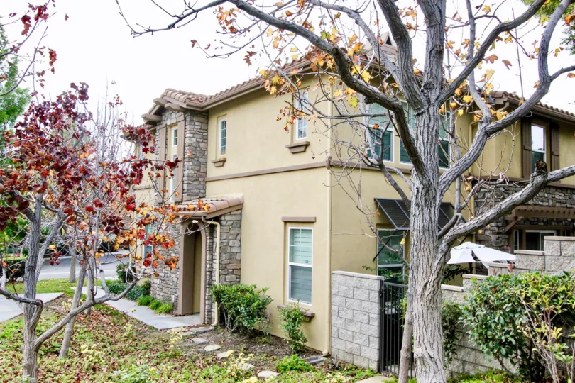 A tan 2 layer house with a rock enterance with many trees surround the area in Centerbury community.