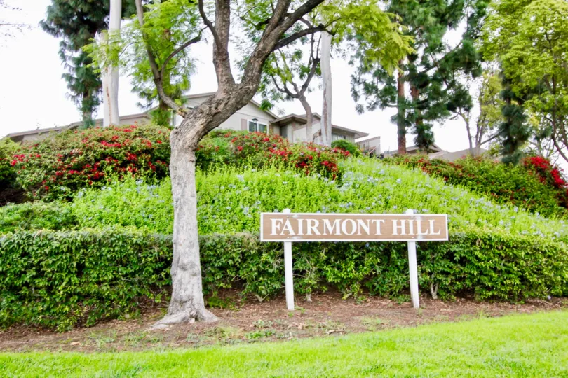 In Fairmont Hill, The board is placed on the pathway with natural trees, lawn and bushes with flowers
