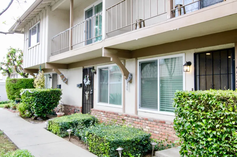 A beautiful white and grey house in the Jamestowne Homes with beautiful ornamental plants and big trees near the road side.