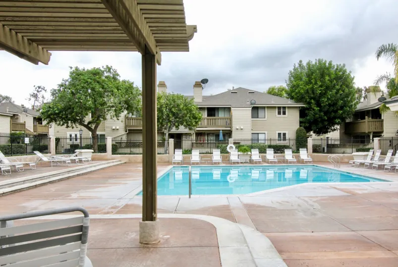 A fenced in pool in Kellogg Terrace with deck chairs on a cloudy day.