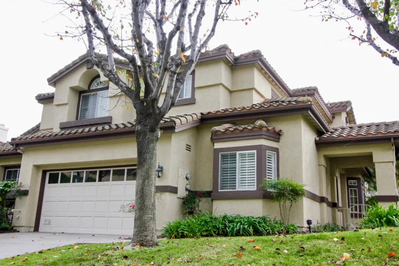 A big beautiful house in the La Terraza I with glass windows and big trees, green grass, shrubs and flowering plants.
