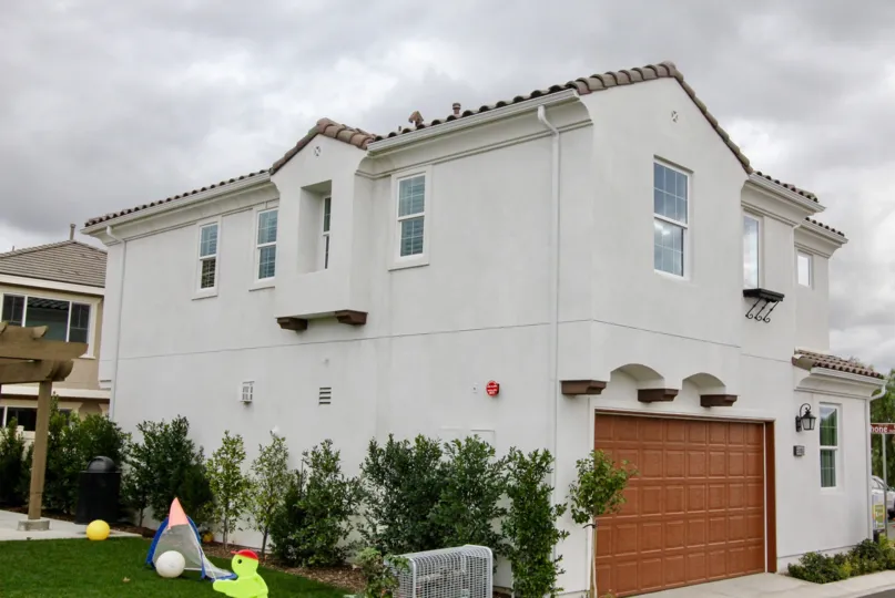 A white color house alone and it has beautiful garden with kids playing things.