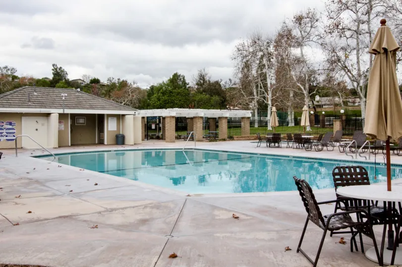 A pool in the Rancho Dominguez Townhomes with deck chairs and tables on a cloudy day.