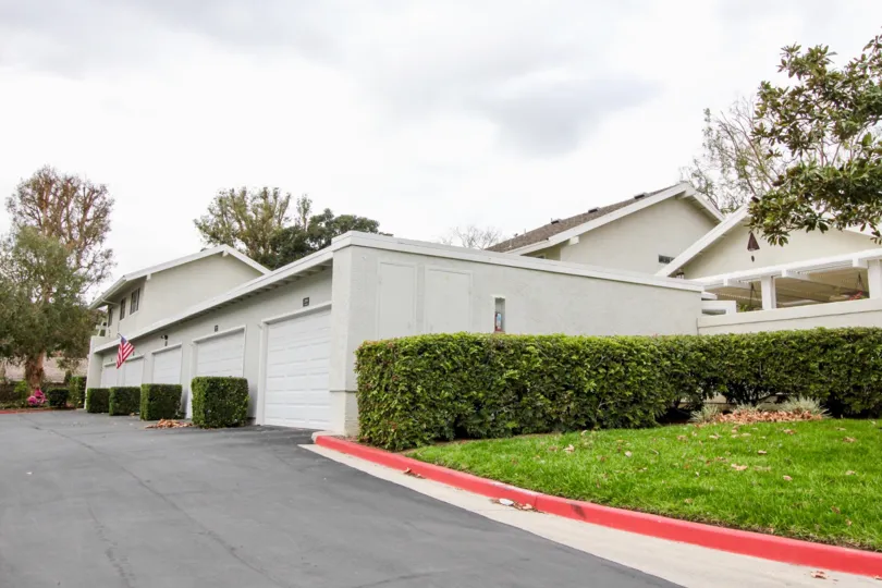The white color buildings in the Rancho Dominguez Townhomes with ornamental plants and green grass near the road side.