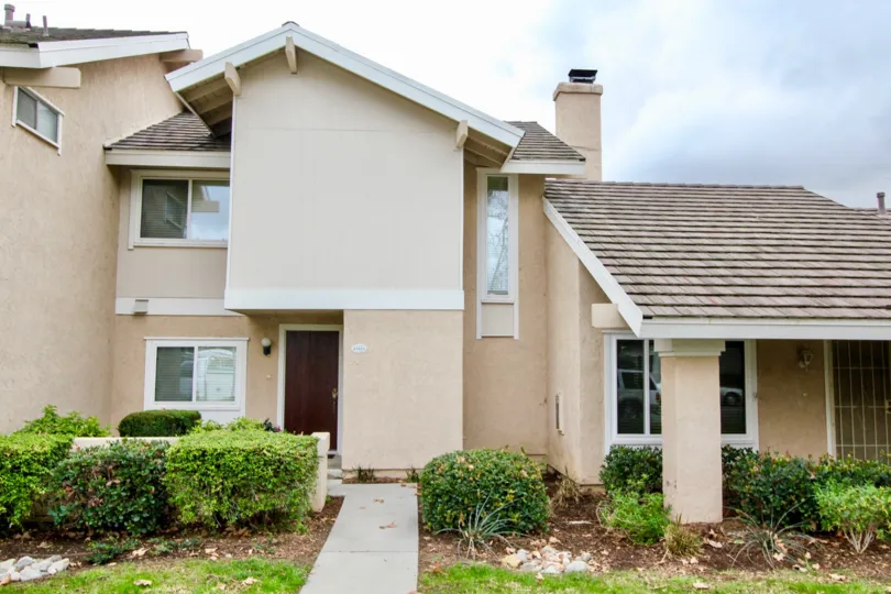 A cloudy day in the Rancho Dominguez Townhomes in front of a house with plants.