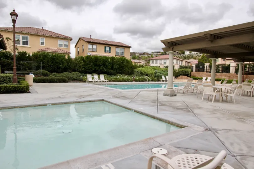 A pool in Villaggio with deck chairs and tables on a cloudy day.