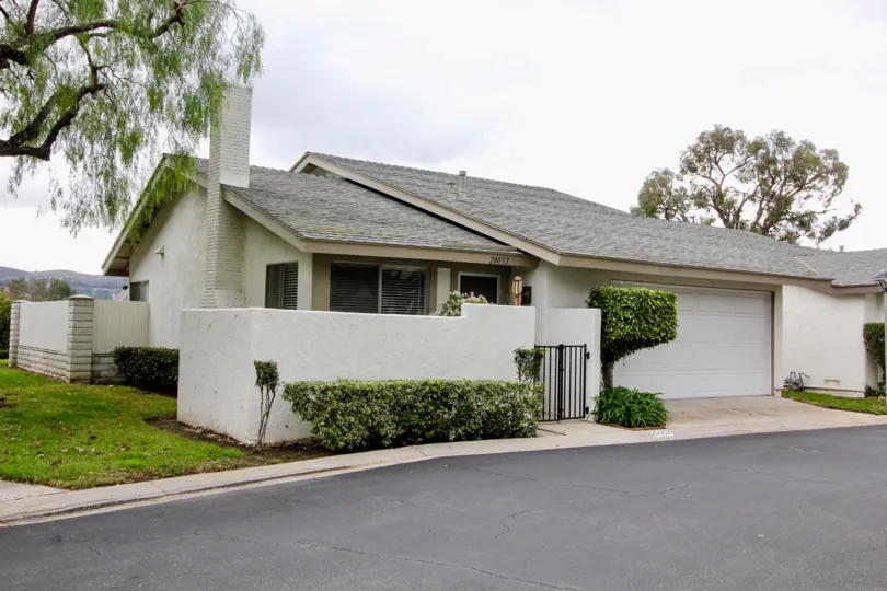 A beautiful white and grey house in the Woodgate with beautiful ornamental plants, big trees, green grass and shrubs near the road side.