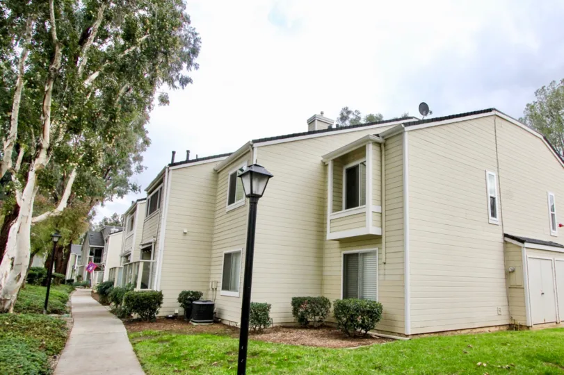 A sunny day in the Yorba Linda Villages with white beautiful building, big trees, green grass and shrubs near the foot path.