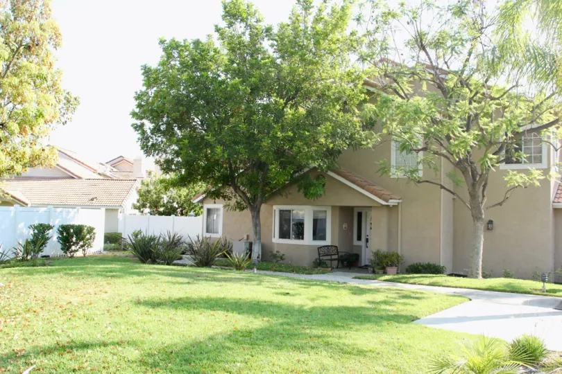 The exterior view of the front of a two story home, partially covered by a large green tree in the Community of Bella Vista in Corona California