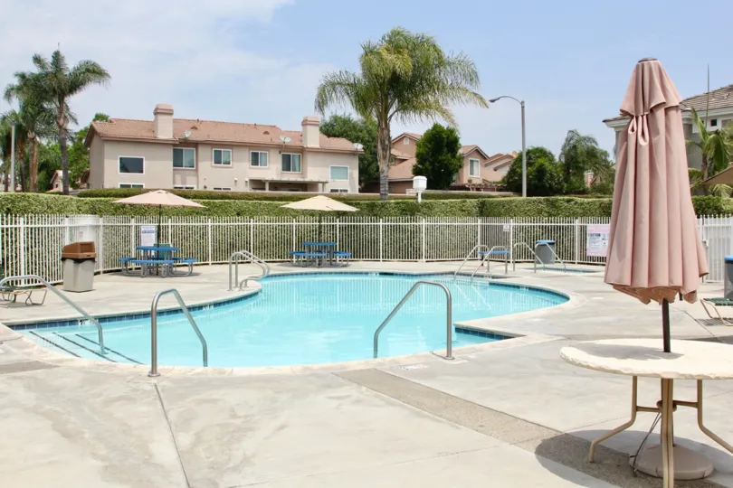 there is a large swimming pool at the front of house with table and chair is surrounded by trees and grasses