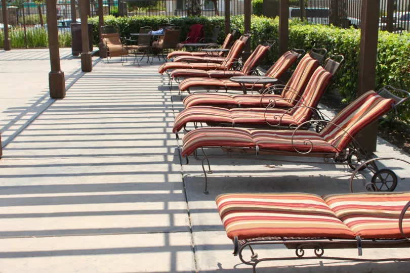Poolside seating that is shaded and modern looking surrounded by the greens