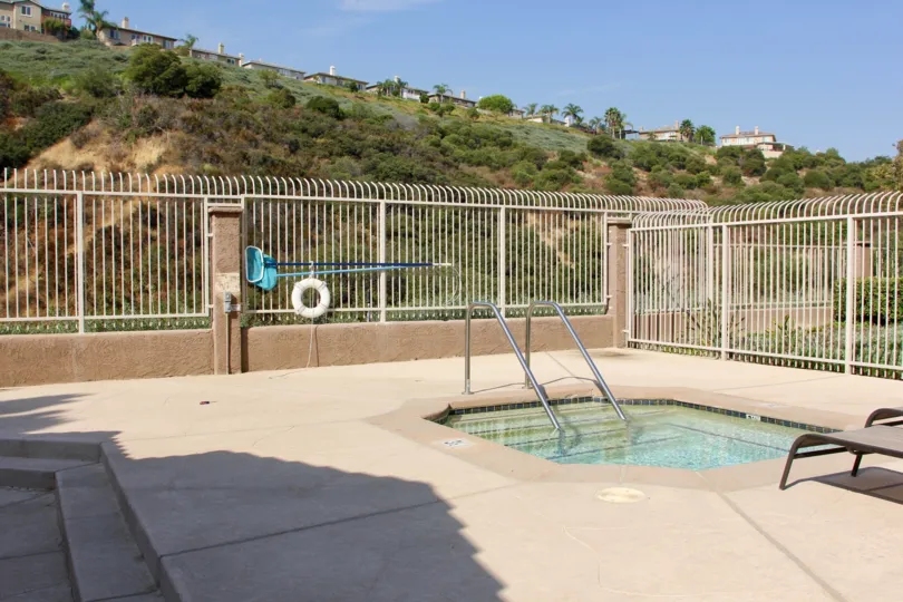 there is a swimming pool and it is a sunny day and house is placed at the top and covered with trees and grasses
