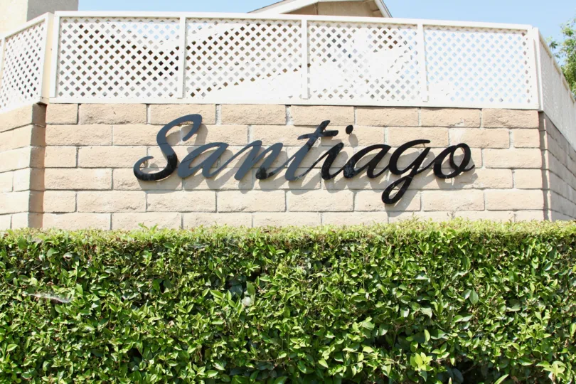 Hedges adorn this brick wall sign of Santiago with green hedges in sunlight
