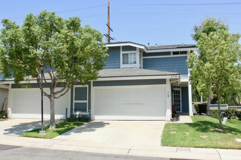 Blue condo with large garage and trees with spotty grass