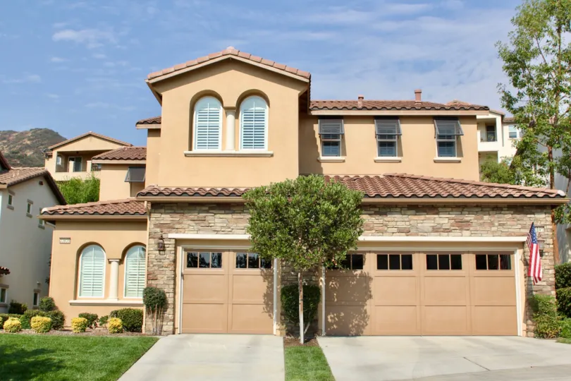 Two garages lead up to the same home with manicured gardens and trimmed hedges