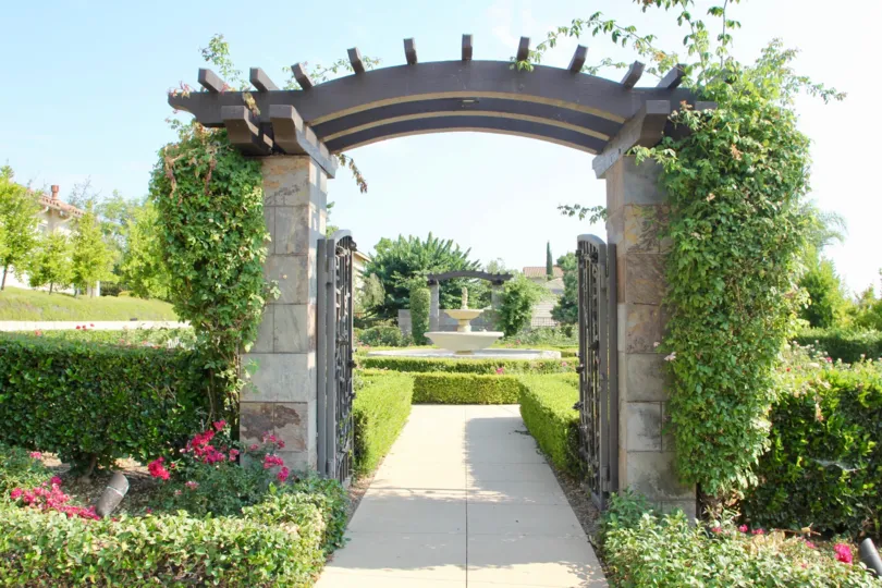 A brown wood, and stone pergola sits above a walkway at Trilogy at Glen Ivy.