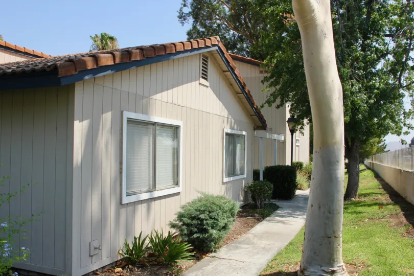 Side of a tan home with exterior side walkway in the Village Grove Cluster community of Corona, California