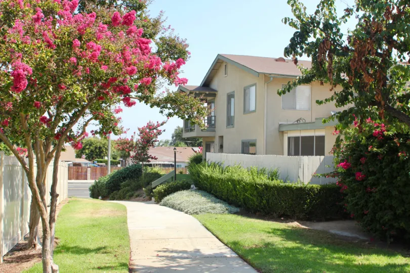 red flowers amidst well mowed greenery of Village Grove Townhomes, Corona, California