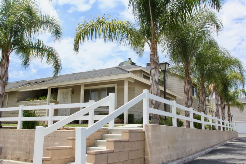 Palm trees line a white fence surrounding a ranch style home in the Lake Country Villas