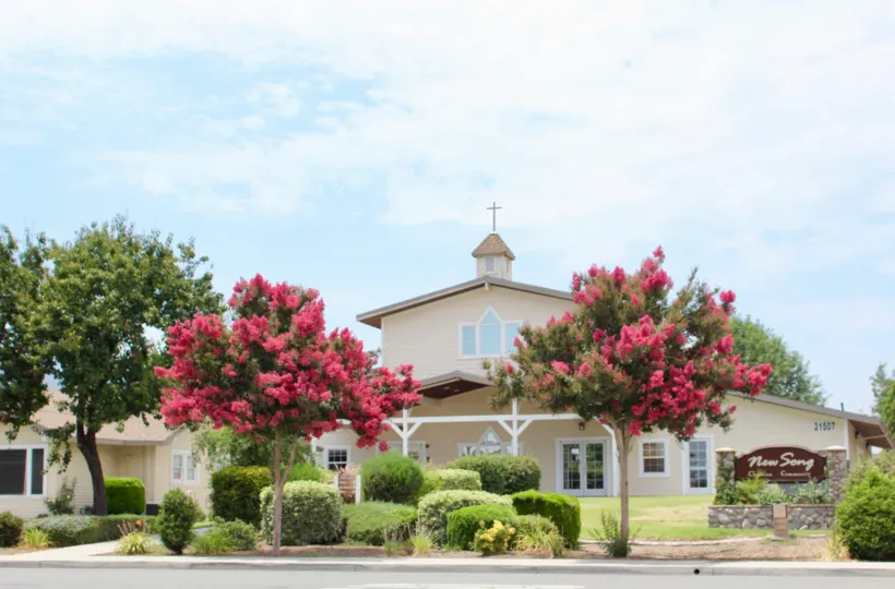 Tan Colored New Song Church Building with pink trees, foliage and bushes