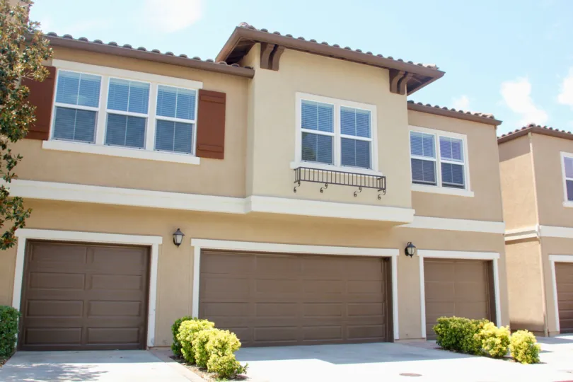 Condo garage with shrubs and large garage doors among trees and gardens